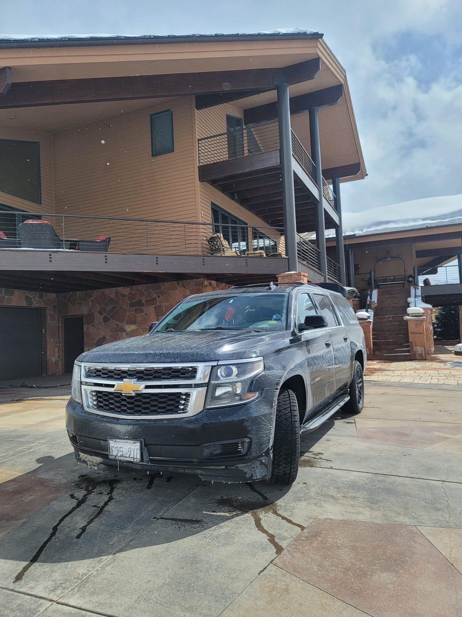 A full-size SUV waiting in the driveway of a Park City home in winter, snow on the roof behind it