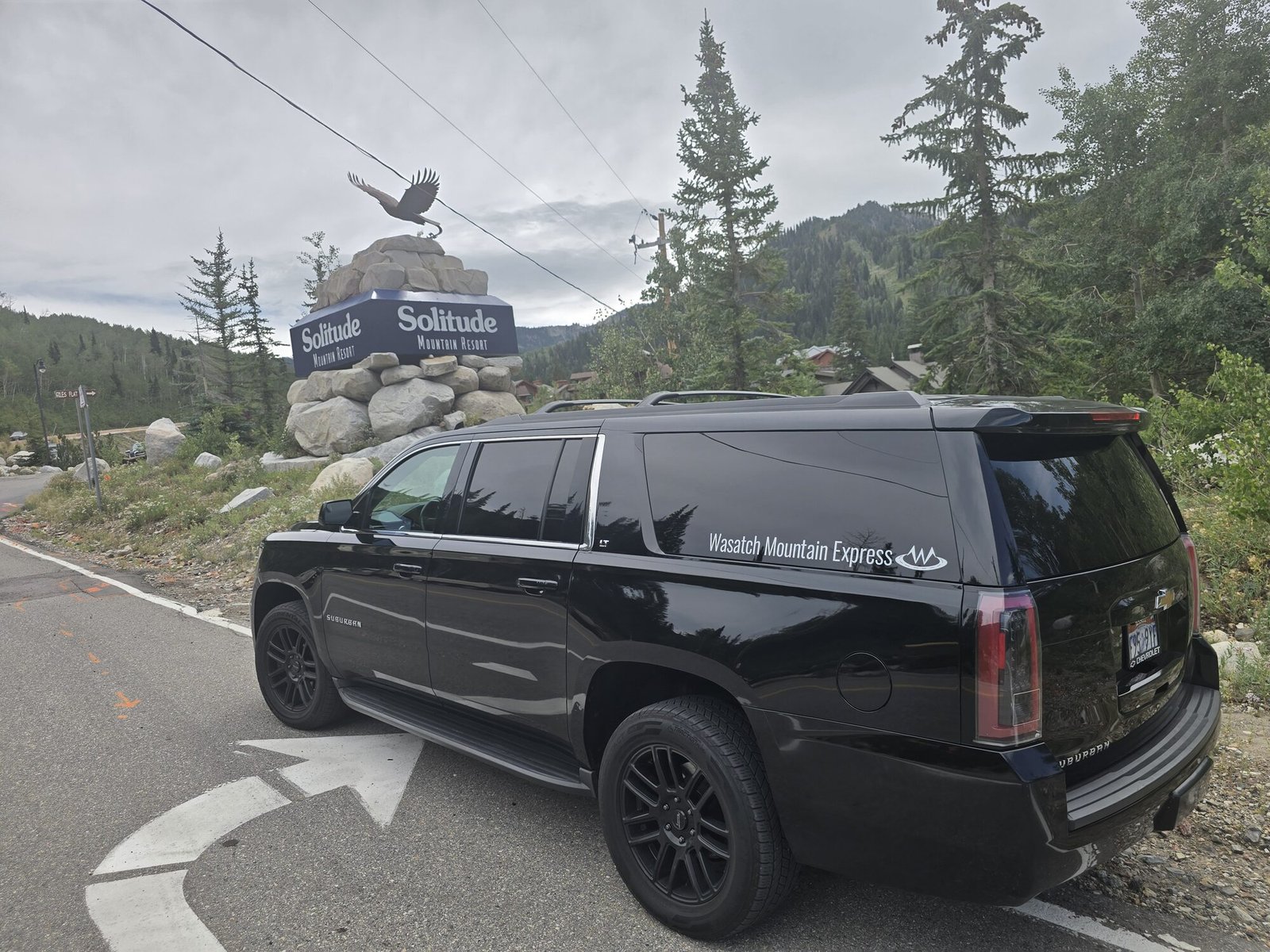A full-size SUV at the Solitude Mountain Resort entrance sign, with pines and the canyon walls behind
