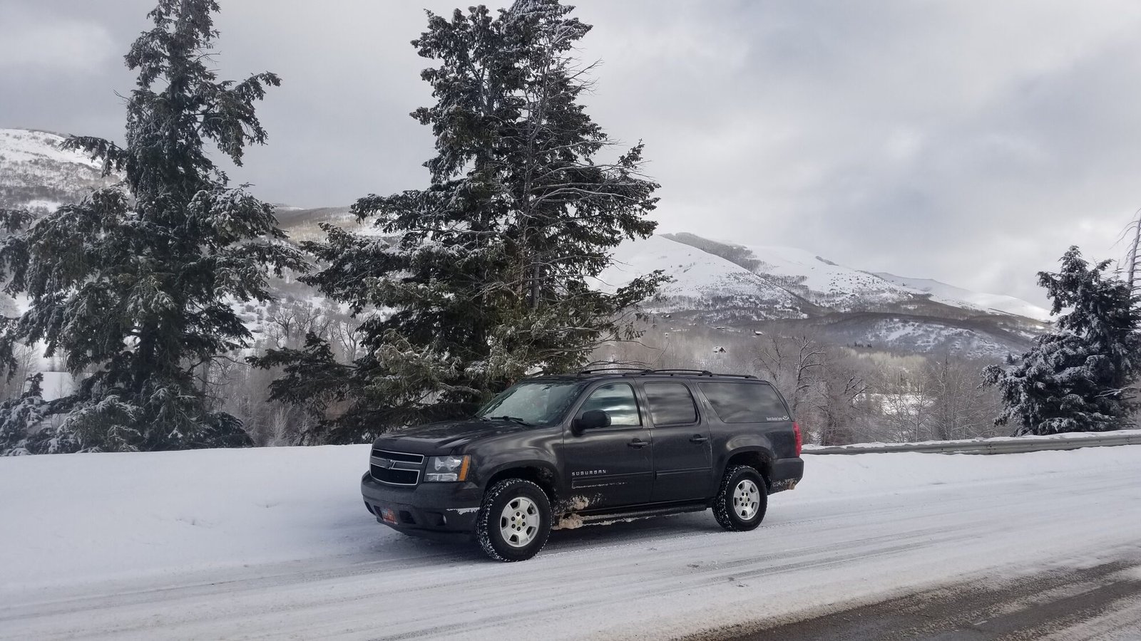 A full-size SUV on a snow-covered road, with snow-laden pines and snowy peaks behind
